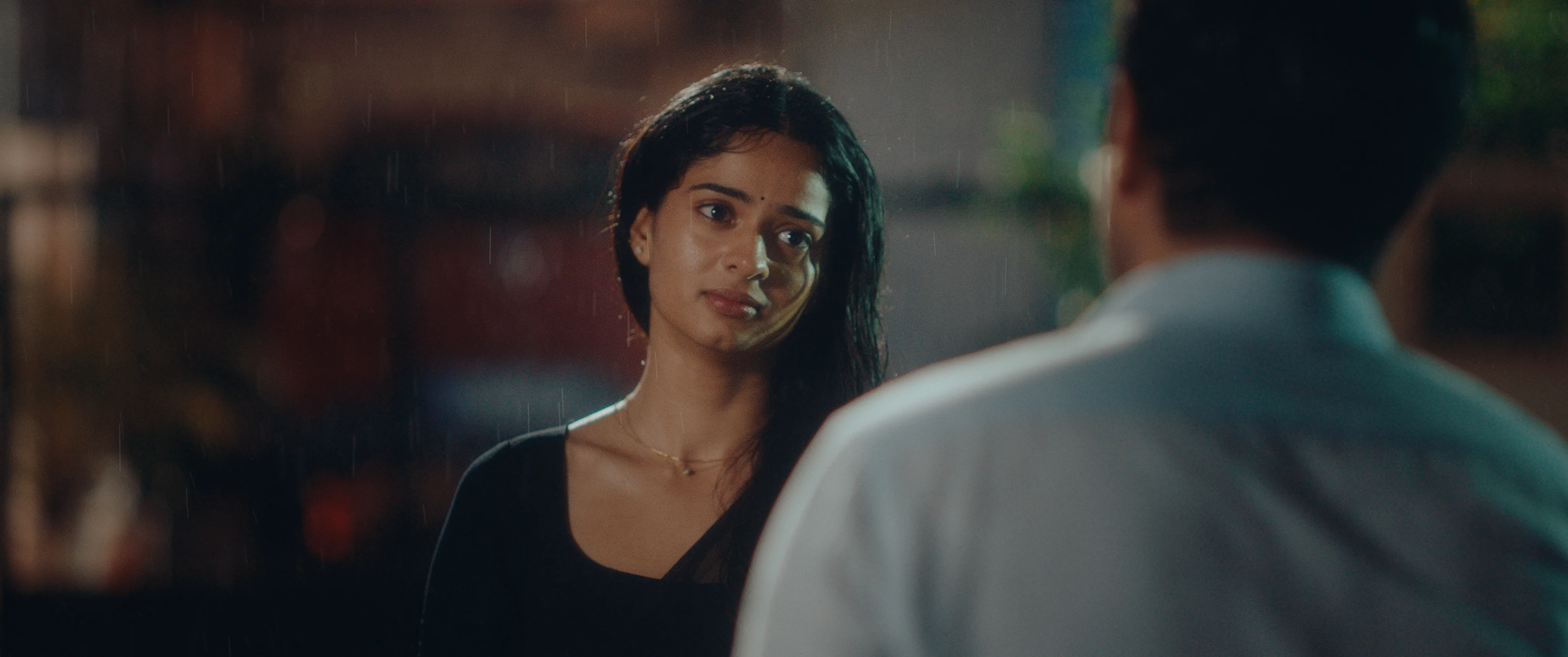 Woman in a black dress speaking to a man in the rain at night.