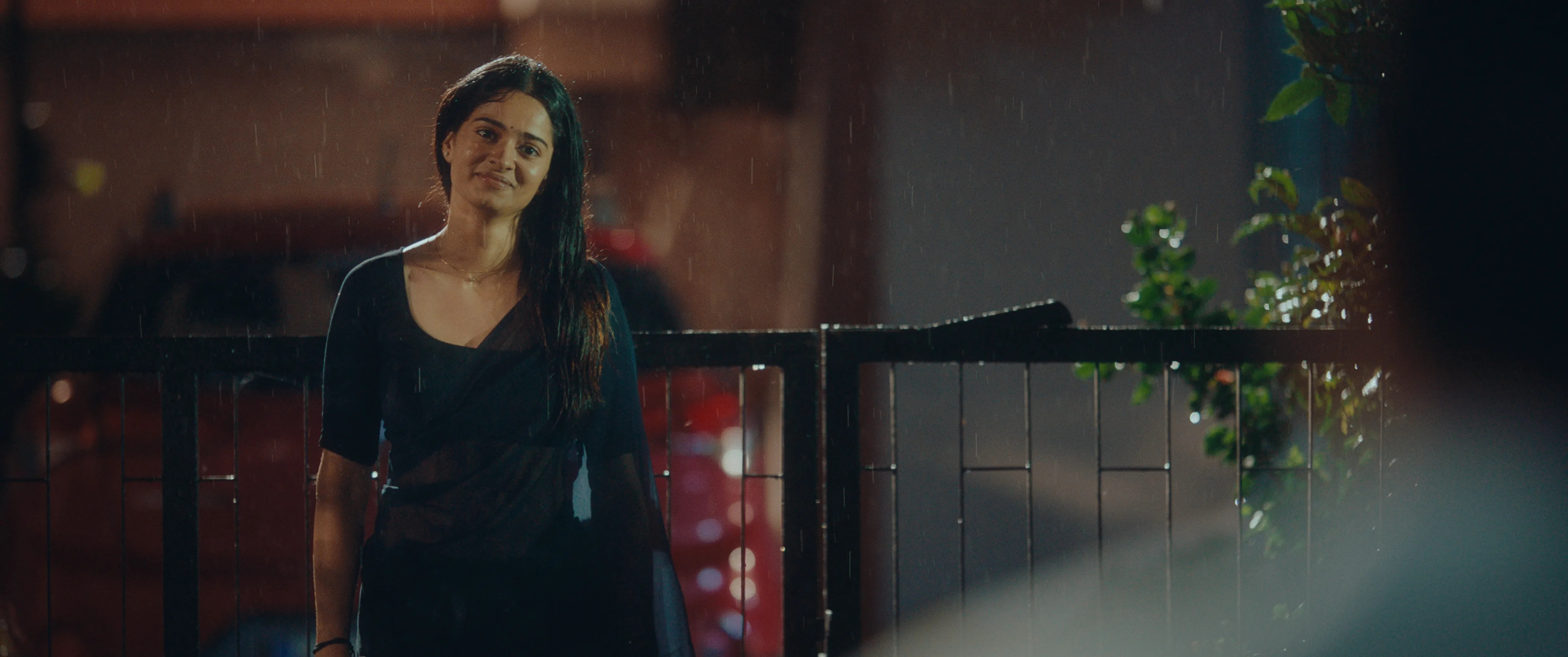Use:  **Woman in a black dress standing near a gate in the rain at night.**