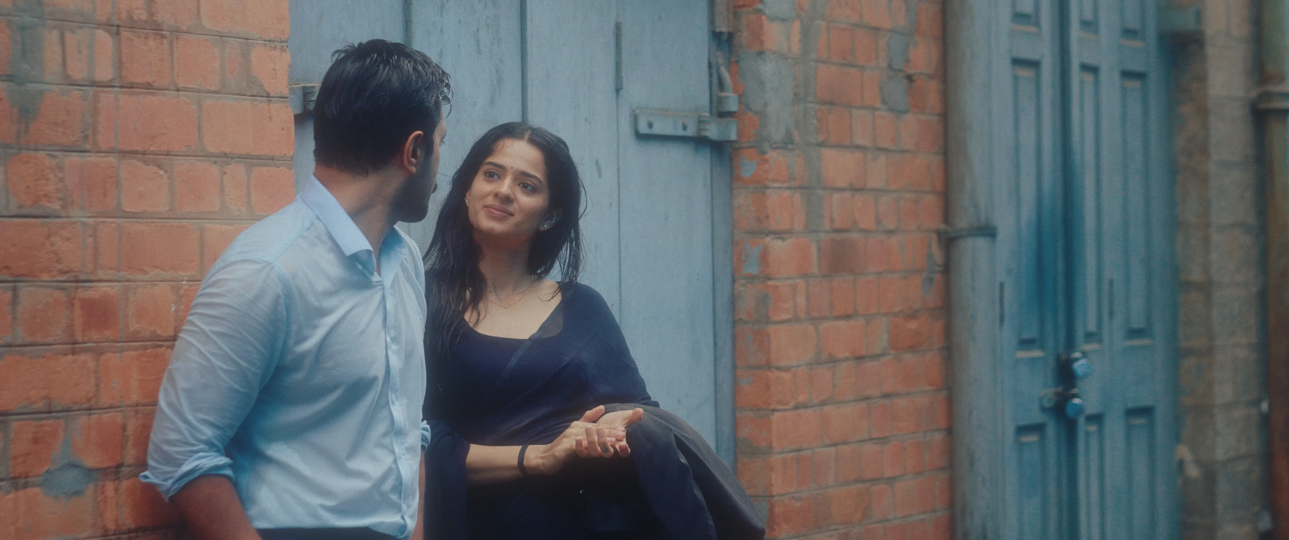 Woman and man sitting together beside a brick wall and blue doorway.