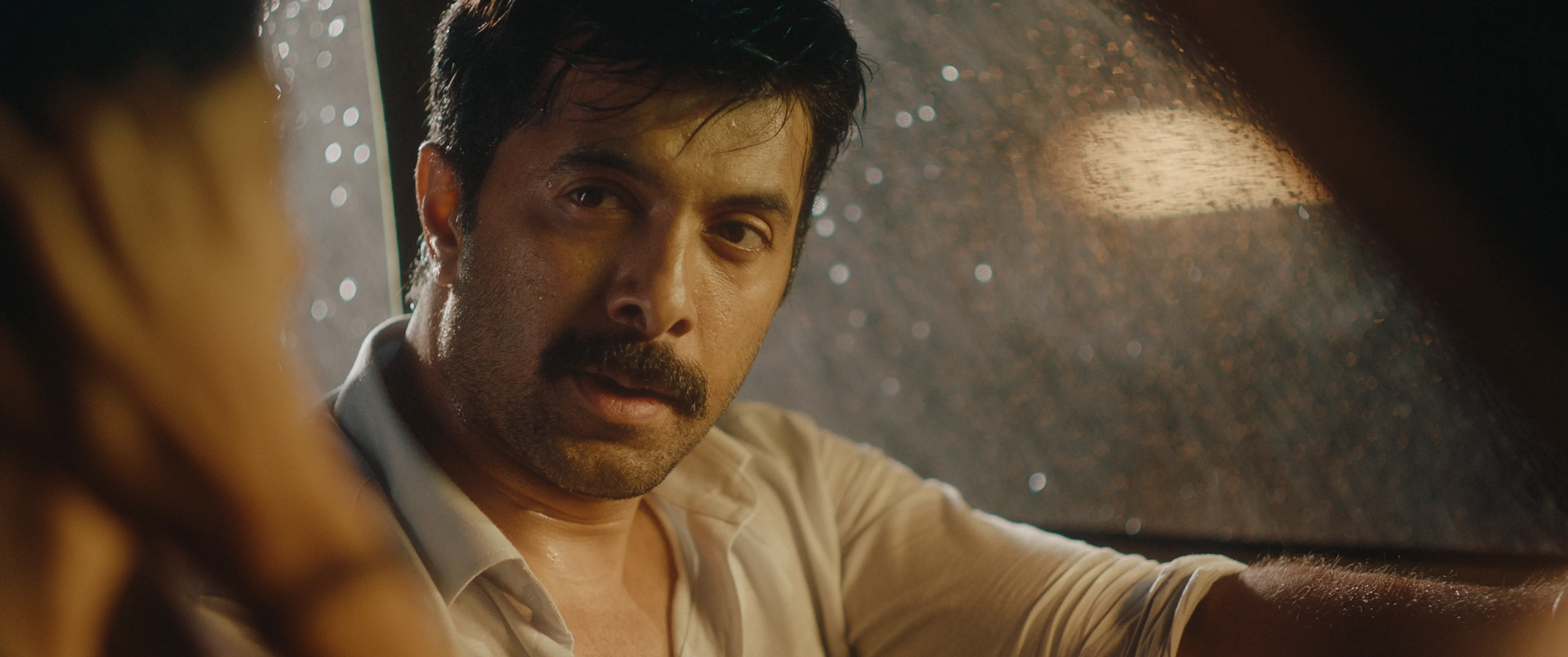 Man in a white shirt speaking to a woman inside a car on a rainy night.