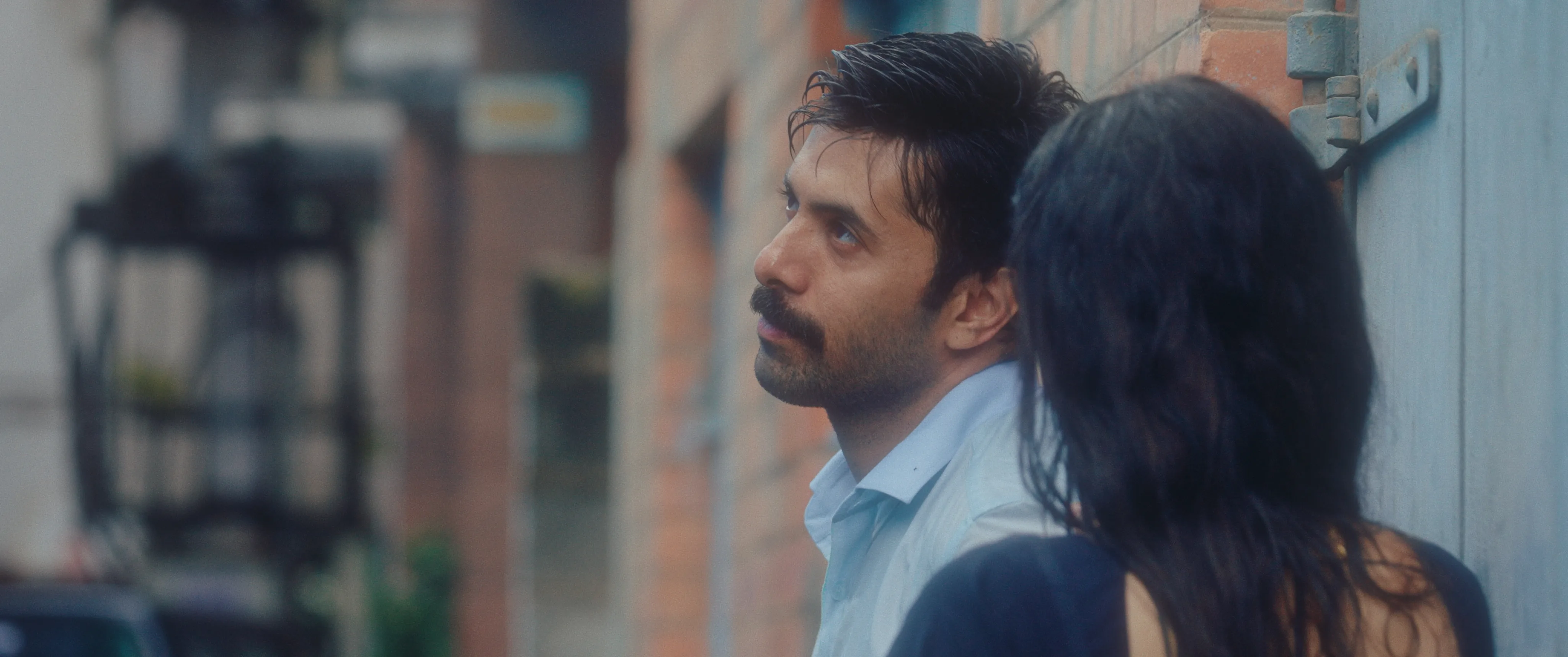 Man and woman sitting together beside a wall, looking upward.