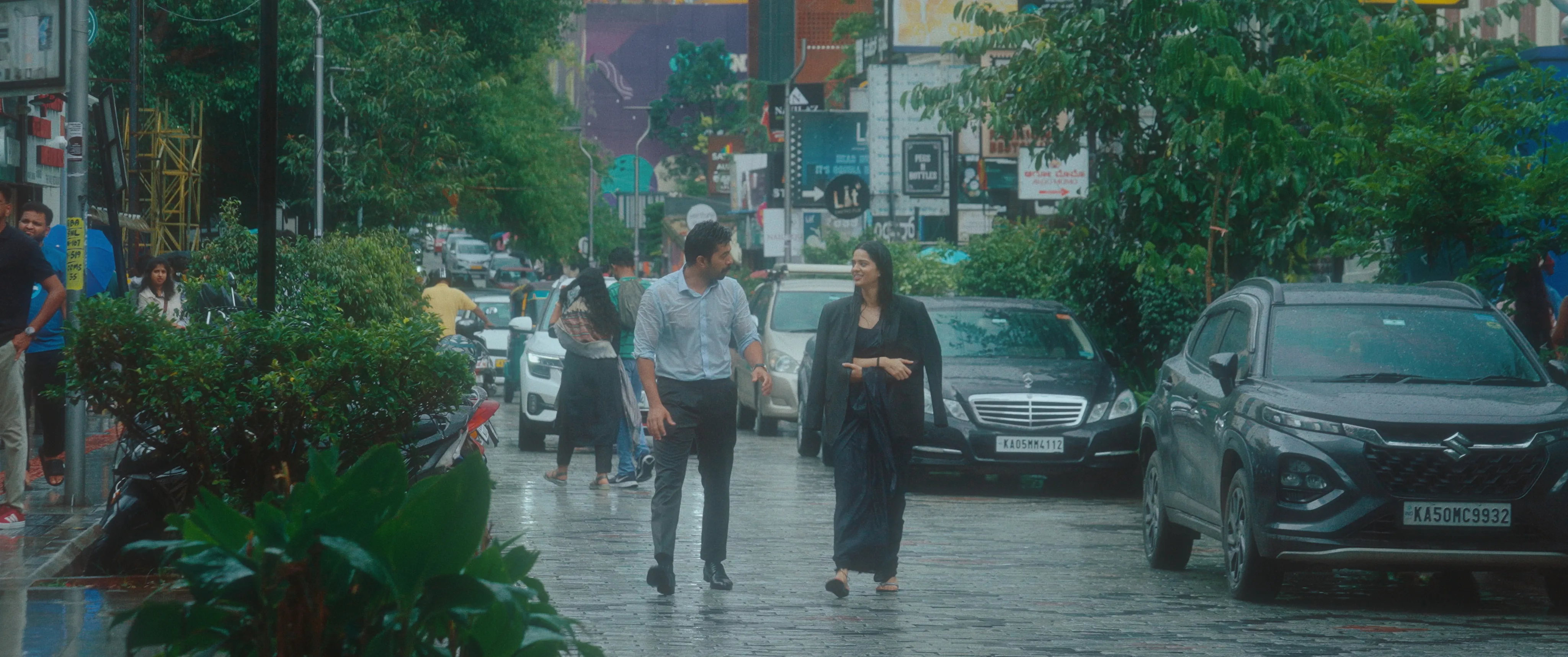 Man and woman walking beside parked cars on a rain-soaked city street.