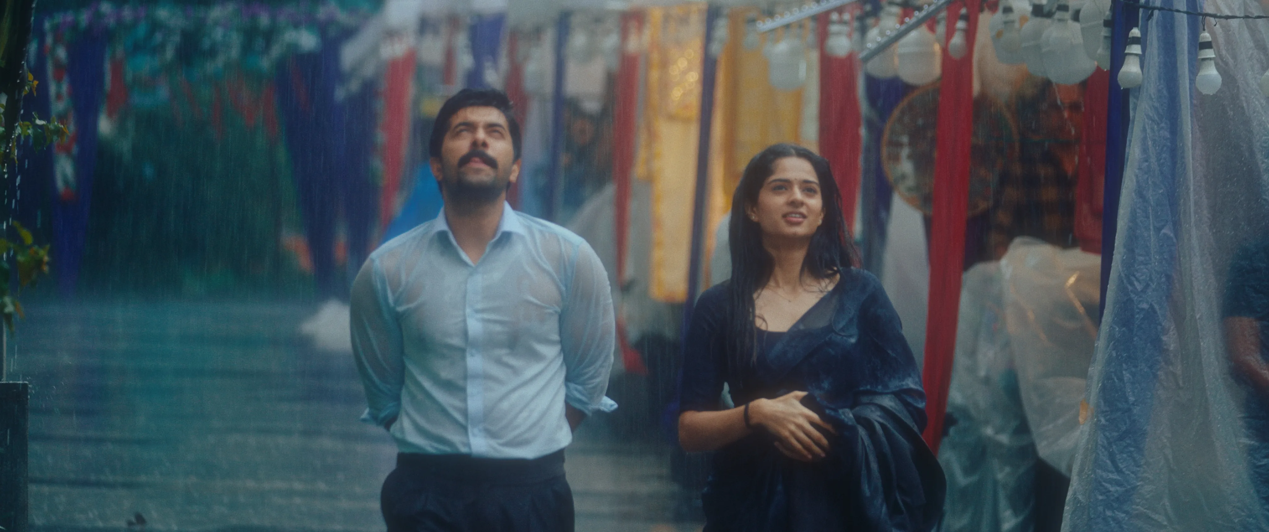Man and woman walking past colorful market stalls in the rain.