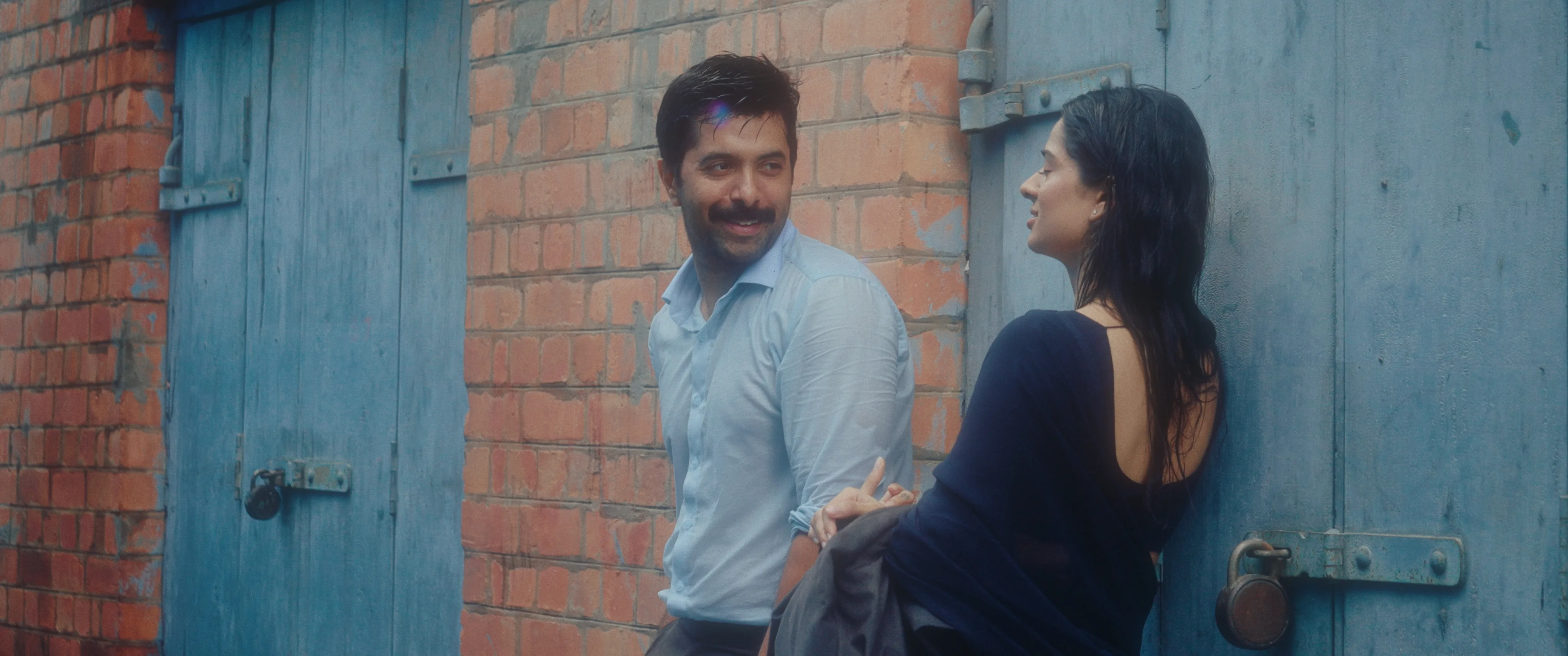 Man and woman talking beside a brick wall and blue doors.