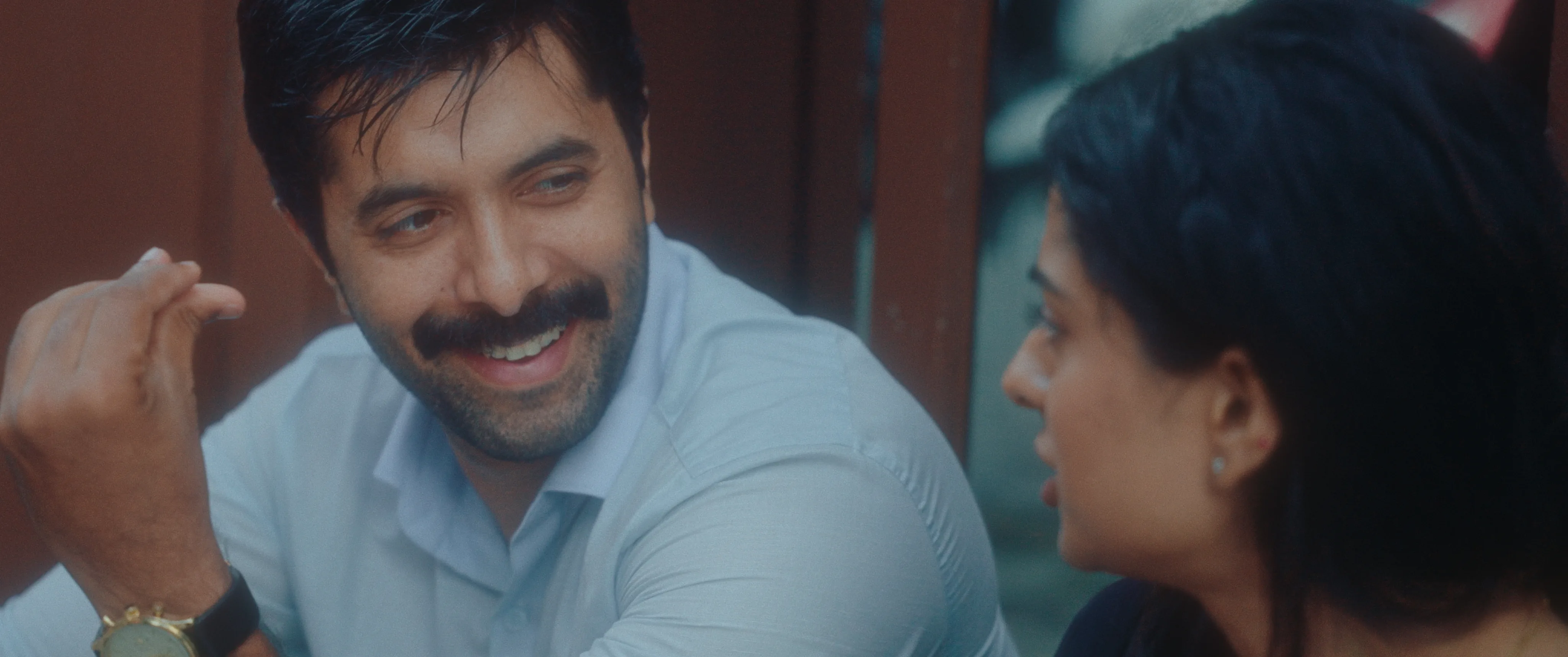 Man smiling at a woman while they sit together outdoors.